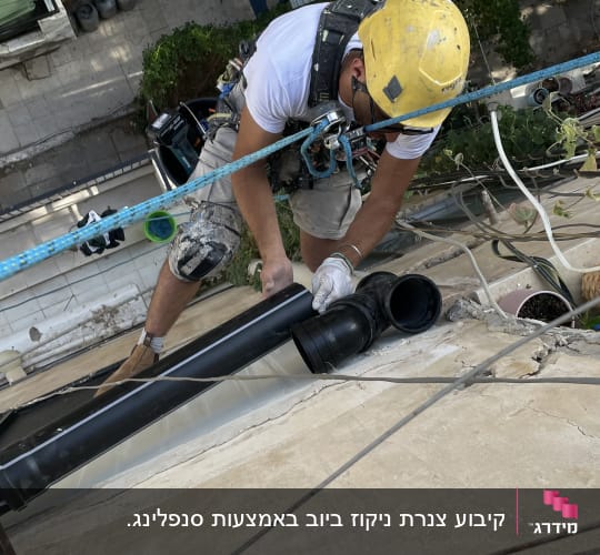 עובד בגובה עם קסדה צהובה מתקין צינור שחור